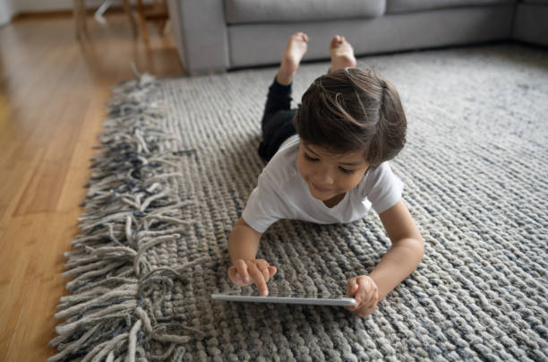 Child lying on a textured area rug while using a tablet in a living room | All Floors Design Centre